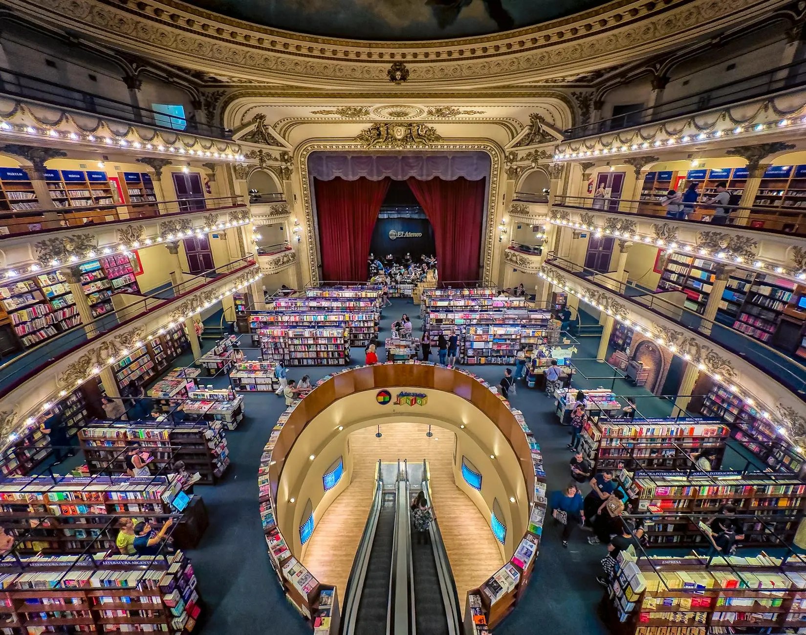 Aerial view of a large bookstore with multiple levels and colorful bookshelves, featuring wooden escalators and people browsing books.