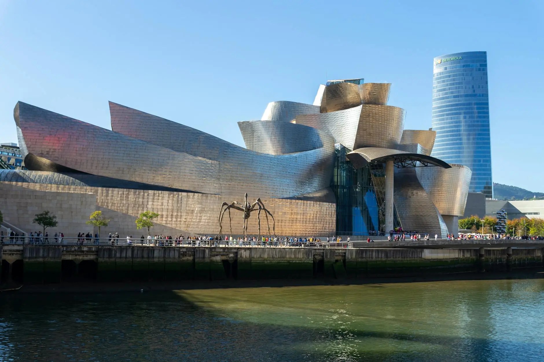 Guggenheim Museum Bilbao exterior with a large spider sculpture in the foreground, reflecting modern architecture and vibrant city life.